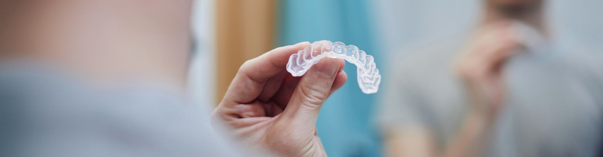 Close-up of a clear orthodontic aligner being held by a dental professional in a dental office.